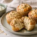 Gylne proteinmuffins med havre på en tallerken, én delt i to for å vise den saftige innsiden, med banan og cottage cheese ved siden av.